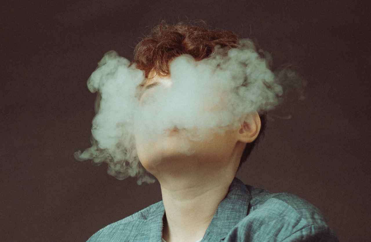 Close-up view of a person exhaling thick vape smoke obscuring their face.